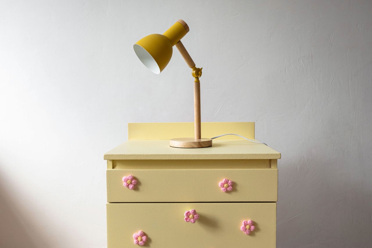 A minimalist view of a yellow lamp on a vintage dresser with floral handles in pastel tones.